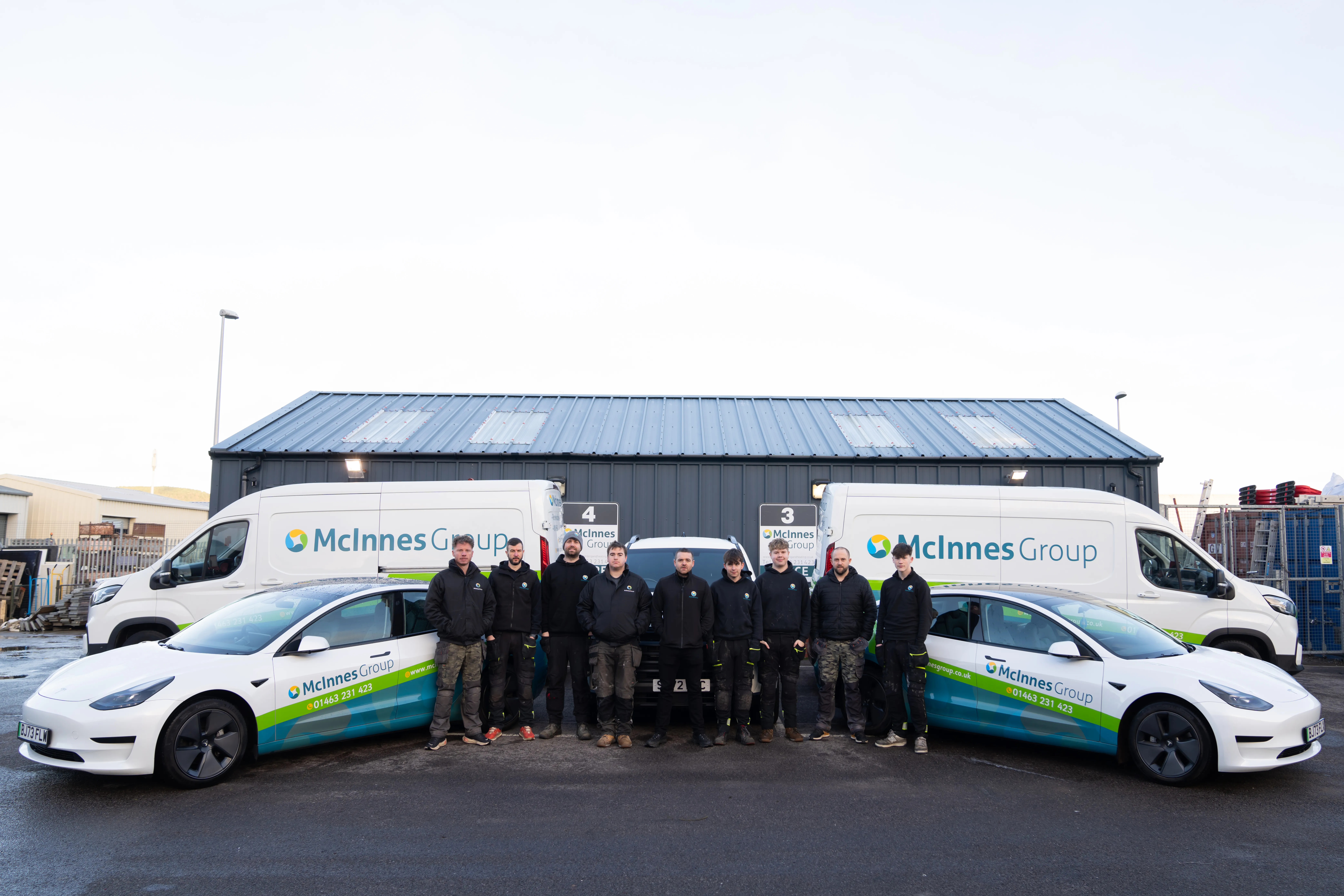 The McInnes Group engineering team lined up in front of the Inverness HQ with branded vans and Tesla Model 3s
